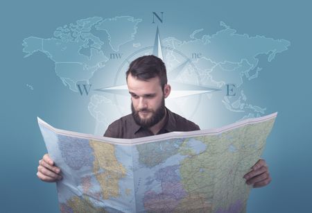 Handsome young man holding a map with a world map and a compass behind him