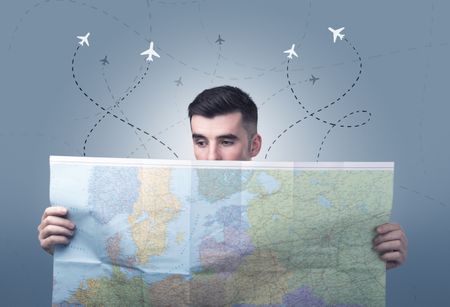 Handsome young man holding a map with little planes and their paths above him 