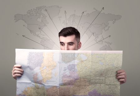 Handsome young man holding a map with world map and arrows behind him