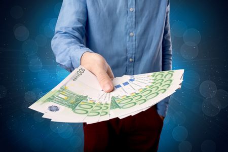 Young businessman holding large amount of bills with shiny blue background