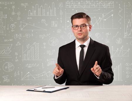 Young handsome businessman sitting at a desk with white graphs and calculations behind him