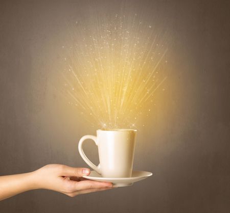 Young female hand holding tea mug with a beam of light rising out of it