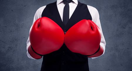 A well dressed sales person standing with red boxing gloves on his hand in front of urban grey wall background concept.