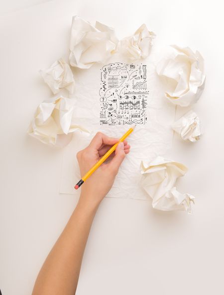 Female hand next to a few crumpled paper balls drawing charts and graphs