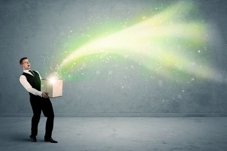 Bright yellow, green light beams escaping a cardboard box held by young elegant male business person in stylish suit concept.