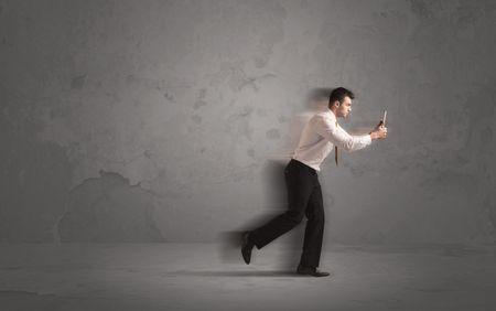 Running businessman in a rush with device in hand on background