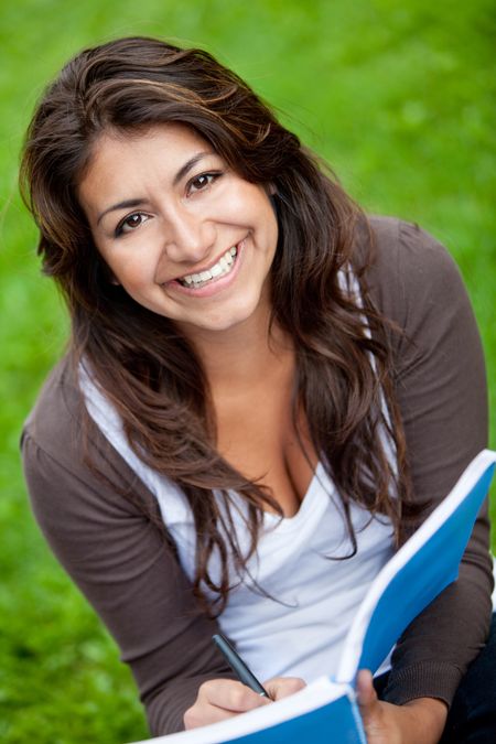 Beautiful female student holding a notebook and smiling outdoors