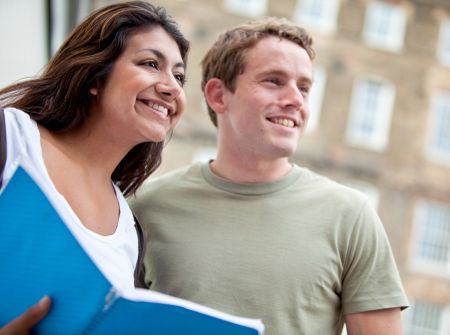 Happy students holding a notebook outdoors and smiling