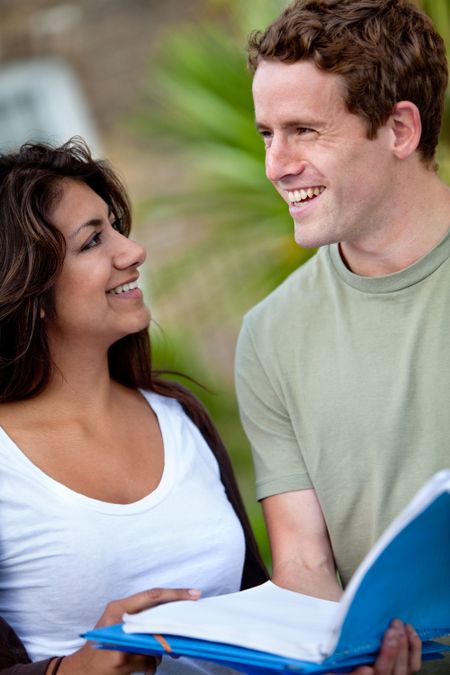 Couple of students with notebooks outdoors and smiling