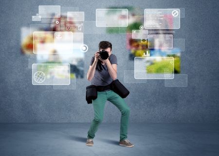 A young professional male photographer holding cameras and taking pictures in front of a blue wall with pictures, icons, text information concept