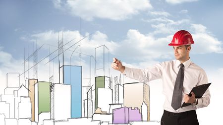 A young construction worker in a red safety helmet happily planning a city sight and drawing lines, arrows, angles, buildings with a pen in his hand