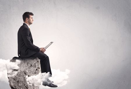 An elegant  smart businessman with laptop sitting in empty grey space on top of a cliff, between clouds concept