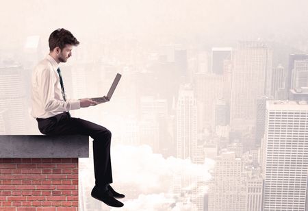 An elegant businessman in modern suit sitting on the top of a brick building, looking over the cityscape with clouds concept