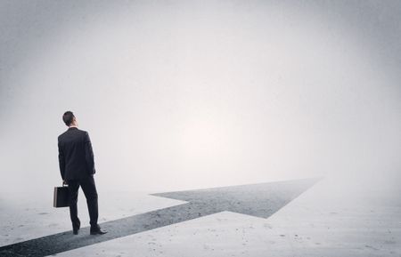 A professional businessman thinking while standing on a black arrow pointing forward in grey space concept