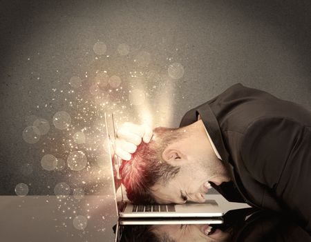 A young depressed business person laying his head on computer keyboard with thoughts exploding from his head illustrated by light beams concept