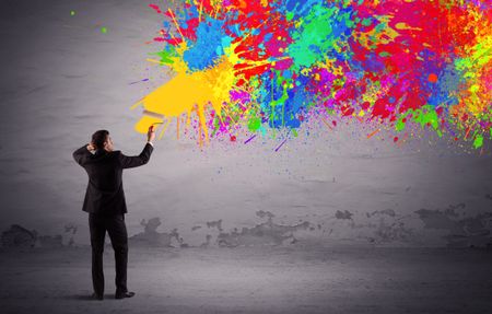 An elegant businessman in suit painting colorful splatter, bright colors on grey urban wall with a paint roller in his hand concept