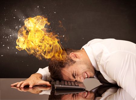 A depressed businessman banging his head in a keyboard and shouting with his head on fire, reflecting on desk