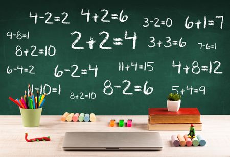 Going back to school concept with blackboard full of numbers and a busy student desk