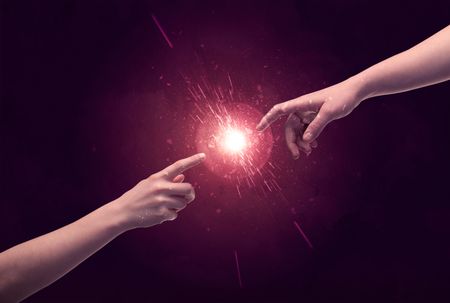 White caucasian male hands reaching out with fingers almost touching in bright red light sparkle in empty space background concept