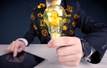 An office salesman promoting his bright ideas concept with illustration of online media and device logos around electric glass light bulb.