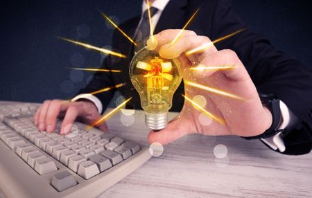 A male business person holding an electric light bulb in his hand with beam rays illustration concept.