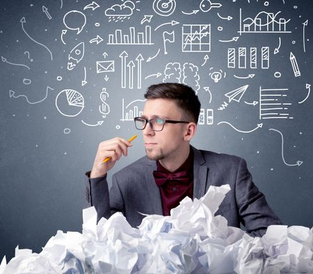 Young businessman sitting behind crumpled paper with mixed drawings over his head