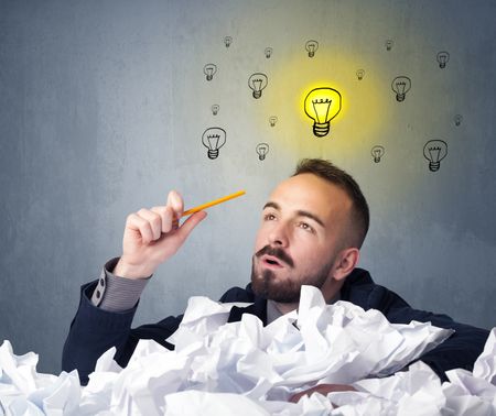 Young businessman sitting behind crumpled paper with lightbulbs above his head