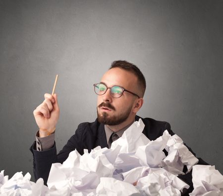 Young businessman sitting behind crumpled paper with grey background 