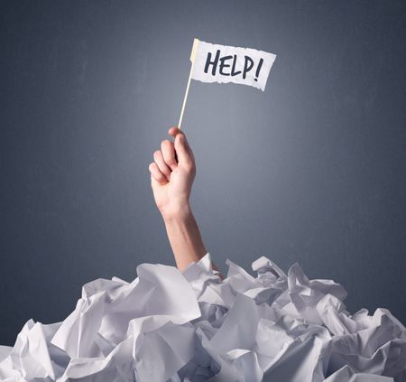 Female hand emerging from crumpled paper pile holding a white flag with help written on it