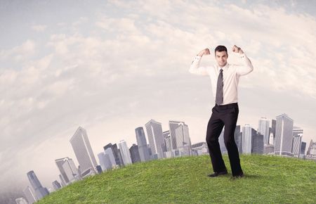 A successful male good looking business man standing in small green grass in front of city landscape with skyscrapers concept.