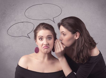 Two girls chatting and sharing their secrets concept with drawn chat bubbles on the background urban wall.