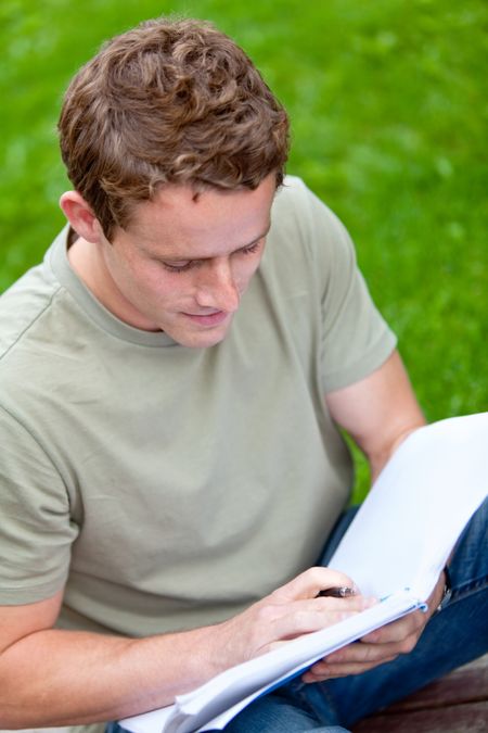 Male student outdoors reading from a notebook