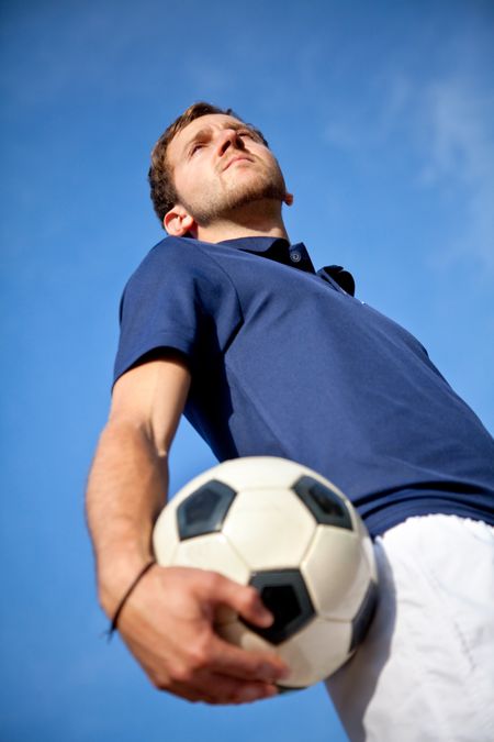 Man holding a football outdoors with the sky on the background