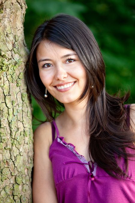 Beautiful woman portrait outdoors leaning on a tree and smiling