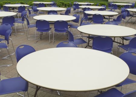 Identical round white tables and hard blue chairs grouped for outdoor gathering on patio
