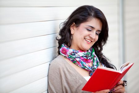 Happy woman holding a book and reading outdoors