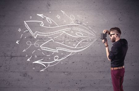 A hipster guy opening his point of view through looking a vintage camera concept with illustratied drawn arrows on urban wall