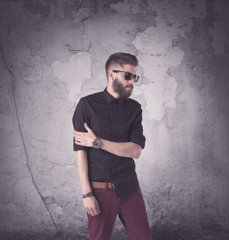 Funny vintage guy with long beard and stylish hair standing in front of urban concrete wall concept
