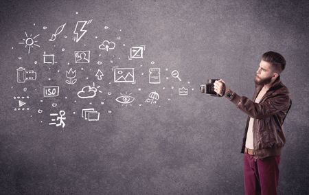 An elegant hipster guy trying to use a vintage camera with camera settings icons drawn on wall, like flash, white balace or ISO value concept