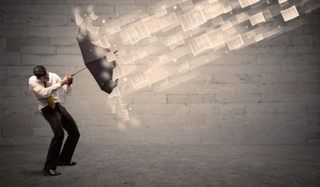 Business man protecting with umbrella against wind of papers concept