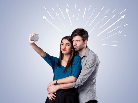 A cheerful young couple taking selfie photo with mobile phone and white lines and arrows pointing to the sky above them concept