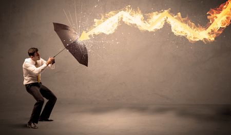 Business man defending himself from a fire arrow with an umbrella on grungy background