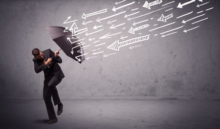 Business man standing with umbrella and drawn arrows hitting him on grungy background