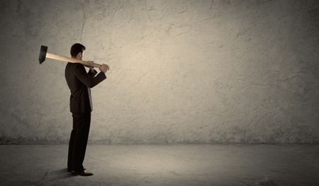 Business man standing in front of a grungy copyspace wall with a hammer