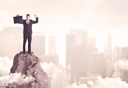 A professional winner business person standing on a dangerous mountain top above the city scape with clouds concept