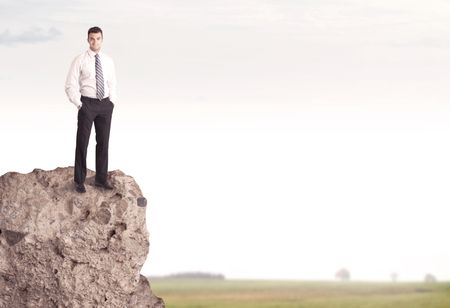 A successful good looking business person standing on top of a high cliff above country landscape with clear white sky concept