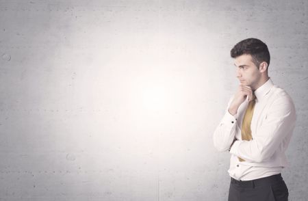 Young sales business person in elegant suit standing in front of clear empty grey wall background while talking on the phone