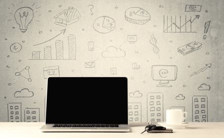 An open laptop on a white office desk with flower, coffee, books in front of wall background full of financial business charts concept