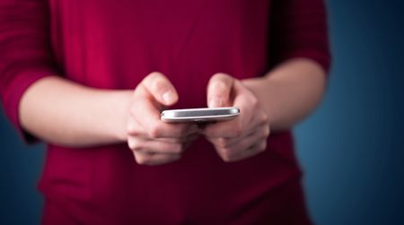 Young woman holding smarthphone in hand while typing