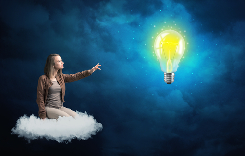 Caucasian woman sitting on a white fluffy cloud looking and wondering at a big, bright, shiny, glowing yellow lightbulb